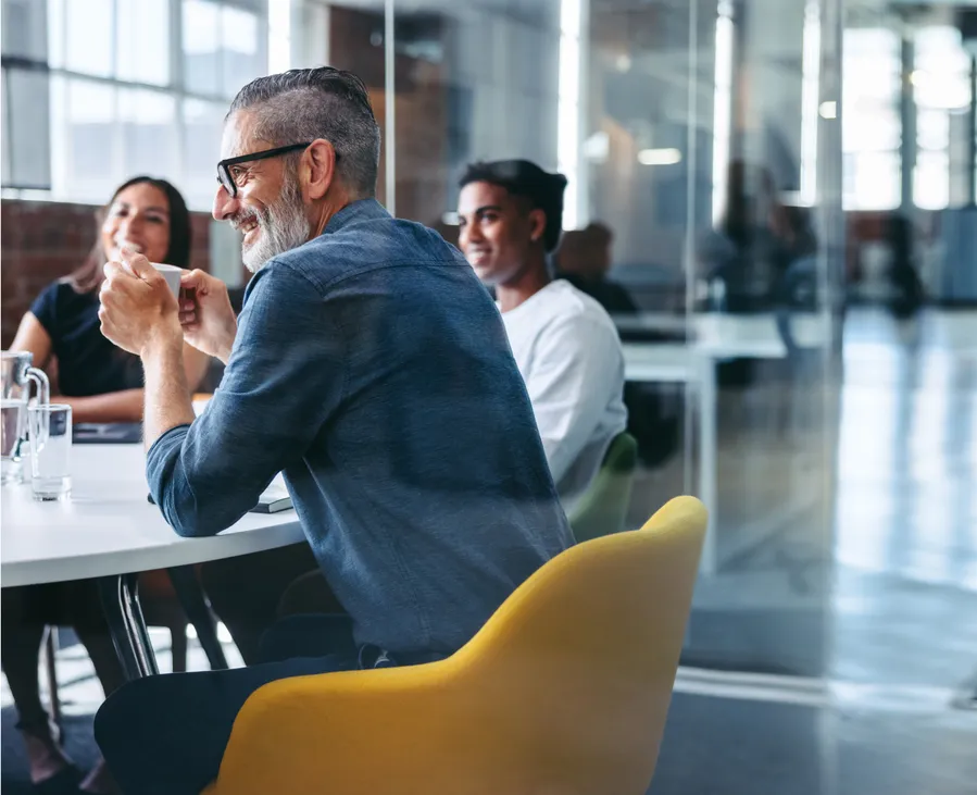 Creative and smiling colleagues attending a brainstorm meeting together in a modern and bright office with glass doors.