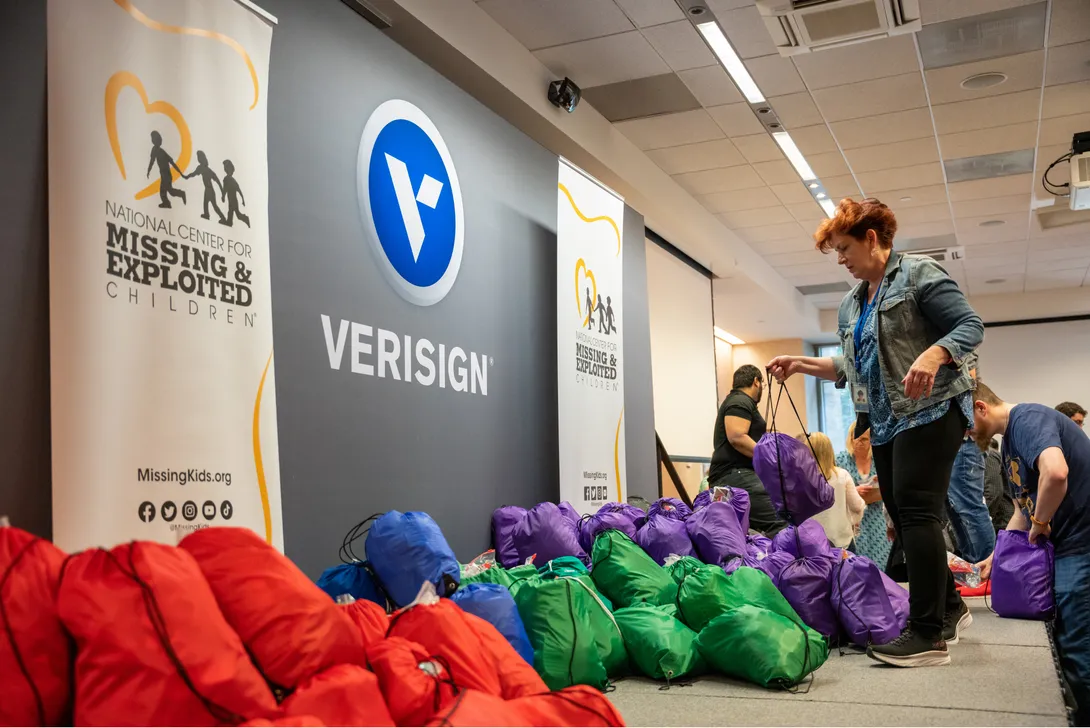 Red and yellow backpacks full of supplies set down under a Verisign and National Center for Missing and Exploited Children logos.