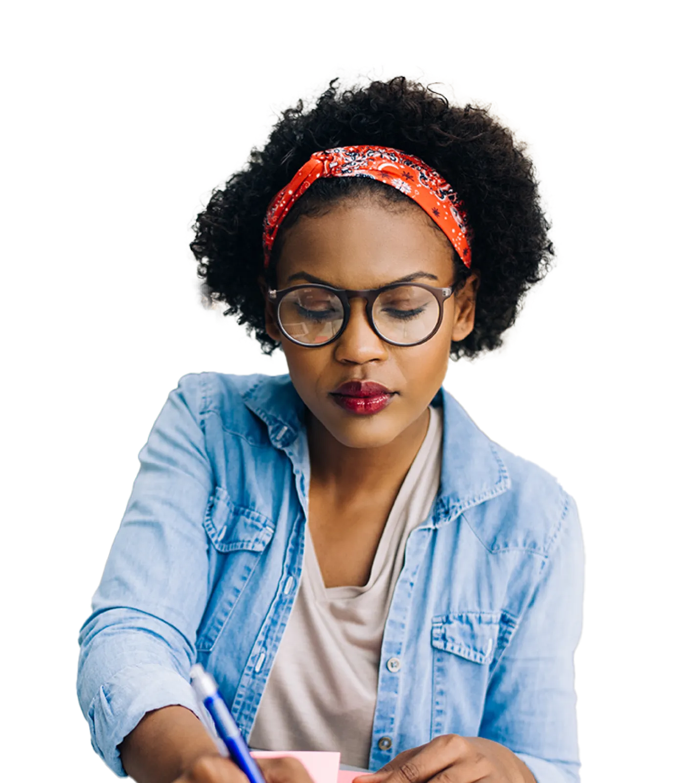 A young woman dressed casually in a denim shirt who’s busy focusing on her work and writing notes in her planner.