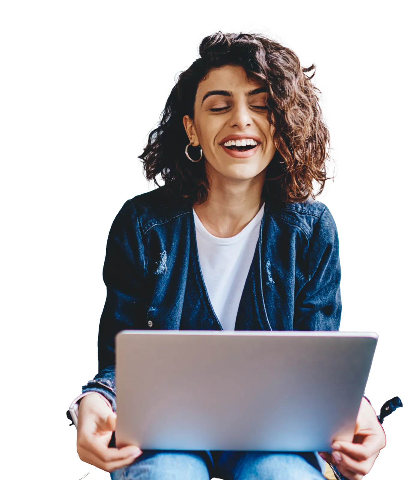 A young woman who is smiling and sitting while holding a laptop and looking down at the screen.