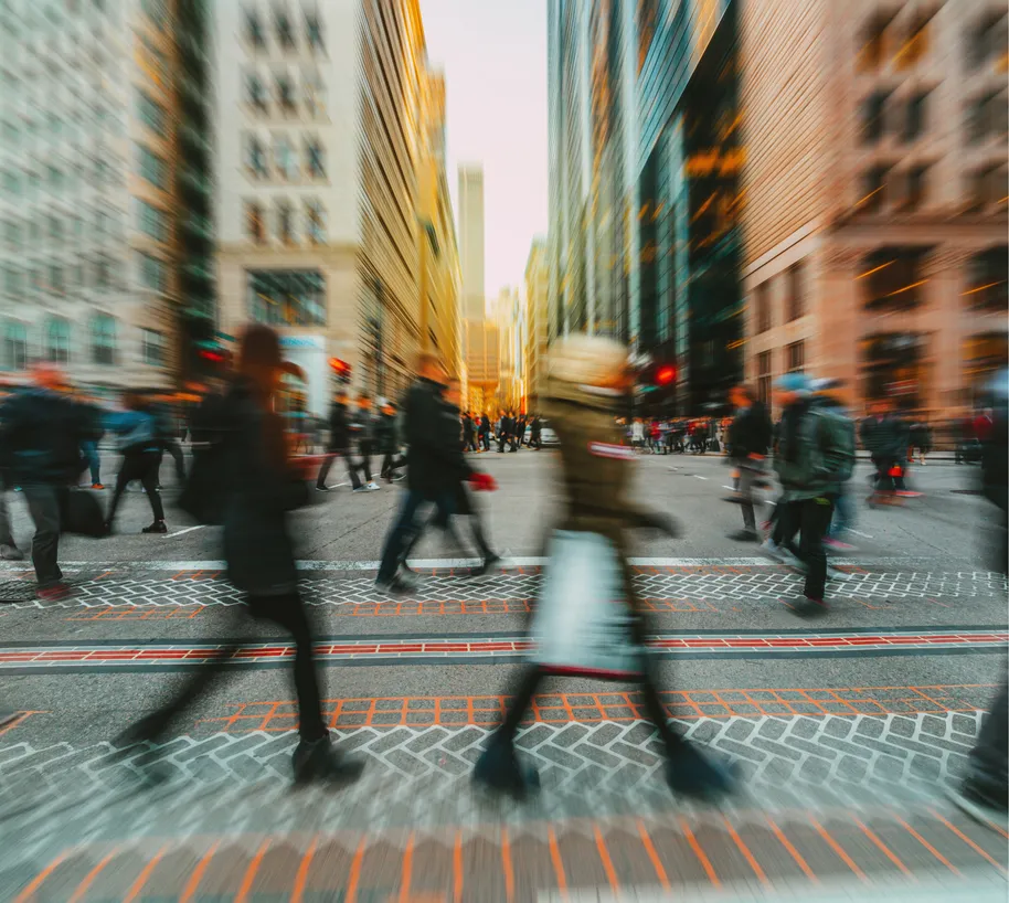 Blurred crowd of pedestrians walking during rush hour with the sun setting in a city.
