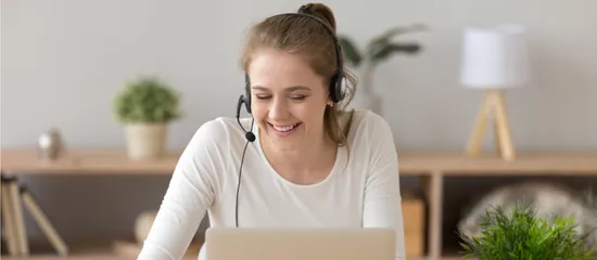 Smiling woman wearing a headset in front of her laptop.